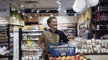 Özel üniformalı bir adam marketteki bir arabaya meyve taşır..