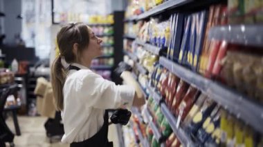 Siyah önlüklü kız işçi raflardaki malları düzenliyor. Malları bir yerden bir yere nakledeceğiz. Mal envanteri.