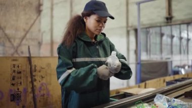 Afro-Amerikalı bir kız çöp geri dönüşüm fabrikasında şişe ayırıyor. Kirlilik kontrolü.