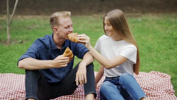 一个女孩和一个男人在野餐时互相喂羊角面包 就像一对夫妇 浪漫的约会快乐 — 图库视频影像