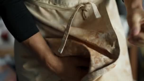 若い幸せな陶芸家は粘土で作業した後 エプロンに手を拭く 接近中だ 伝統的な職業の概念 — ストック動画