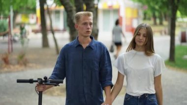 Adam ve kız parkta yürüyorlar, konuşuyorlar. Adamın elinde bir scooter 'ı var. İyi yürüyüşler. romantik randevu.