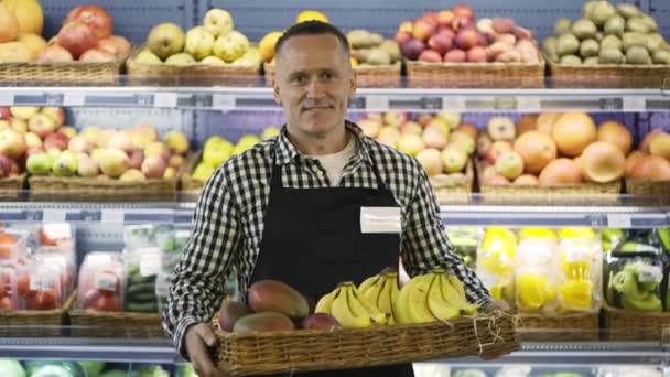エキゾチックな果物の箱を持って幸せな中年の店の労働者の肖像 エプロンにバッジ付きの男 仕事をする — ストック動画
