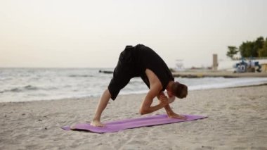 Genç bir adam şafakta spor minderinin üzerinde dururken yoga yapıyor. Özel bir egzersiz yapıyorum. Vücut gerilmesi. Boş zaman, dinlenme..