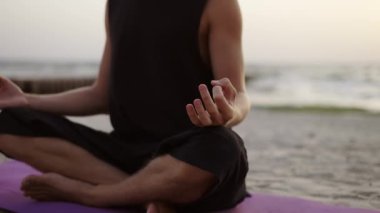 Genç bir adam güneş doğarken yoga yapıyor ve spor minderi üzerinde meditasyon yapıyor. Özel bir egzersiz yapıyorum. Meditasyon, eller. Boş zaman, eğlence zamanı..