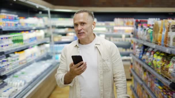 Ein Mann Mittleren Alters Geht Durch Einen Lebensmittelladen Und Spricht — Stockvideo
