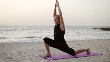 Genç bir adam şafakta spor minderinin üzerinde dururken yoga yapıyor. Özel bir egzersiz yapıyorum. Vücut gerilmesi. Boş zaman, dinlenme..