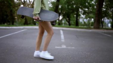 Bir kız elinde kaykayla parkta yürüyor, günlük bir hobi. Parkta yürü, kaykaycıları parka taşı..