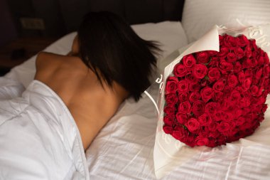 Genç ve seksi Afro-Amerikan kadın iç çamaşırlarıyla kırmızı gül buketiyle yatakta uyuyor.