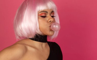 Canlı makyajlı, genç, seksi Afrikalı Amerikalı kadın pembe arka planda sakız şişiriyor.