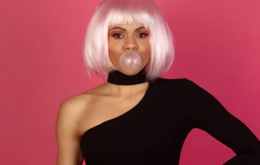 Canlı makyajlı, genç, seksi Afrikalı Amerikalı kadın pembe arka planda sakız şişiriyor.