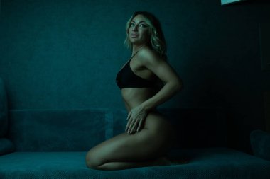 Kanepede siyah iç çamaşırlı seksi sarışın kadın poz veriyor.