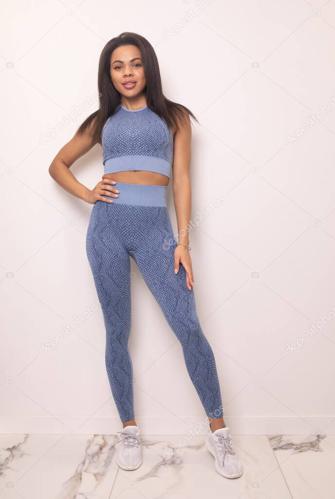 full length view of smiling young fit african american woman in blue sportswear posing in studio