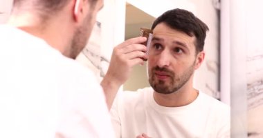 Yakışıklı, gülümseyen genç adam aynaya bakıyor ve tarakla kaşlarını tarıyor.