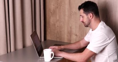 Genç bir adamın işini bitirmesi, bilgisayarını kapatması ve evdeki bardaktan içmesi.