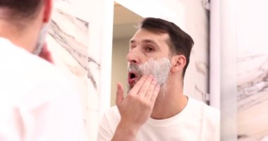 Yakışıklı genç adam banyoda aynaya bakarken yüz jölesi sürüyor ve telefona cevap veriyor.