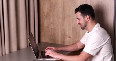 Laptop kullanan ve akıllı telefondan konuşan gülümseyen genç adamın yan görüntüsü