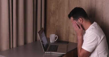Evde dizüstü bilgisayarla çalışan yorgun bir gencin yan görüntüsü.
