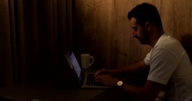 Laptop kullanan, geceleri esneyen ve uyuyan genç bir adamın yan görüntüsü.