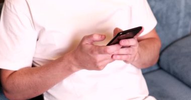 Kanepede oturan ve akıllı telefon kullanan adamın yakın plan görüntüsü.