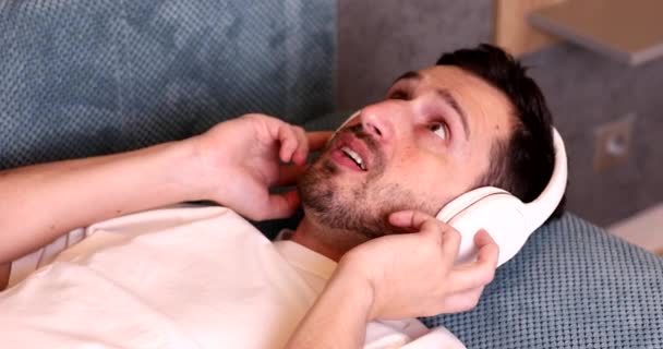Jovem Bonito Fones Ouvido Deitado Sofá Falando Smartphone — Vídeo de Stock