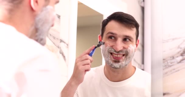 在浴室里用剃须刀刮胡子的英俊微笑的年轻人 — 图库视频影像