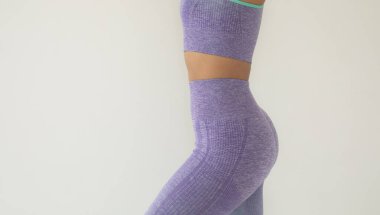 Gri arka planda poz veren mor spor giysili Afro-Amerikan kadının orta bölümü.