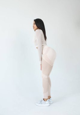 Beyaz spor giyimli, gri arka planda poz veren Afro-Amerikan genç bir kadının yan görüntüsü