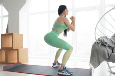 Atletik formda kız oturma odasında elastik bantla spor yapıyor. Ev sağlığı ve sağlık konsepti.