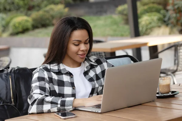 Açık kafede dinlendirici ve bir dizüstü bilgisayar kullanarak bir mutlu genç Afrikalı kadın portresi.