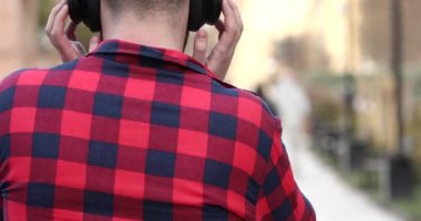 Kulaklıkla müzik dinleyen ve sokakta yürüyen kareli tişörtlü genç adamın arka planı.