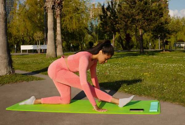 Pembe taytlı güzel siyah bir kadın ve şehir parkında yoga yapan bir kadın..