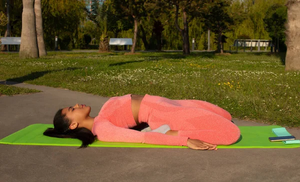 Pembe taytlı güzel siyah bir kadın ve şehir parkında yoga yapan bir kadın..