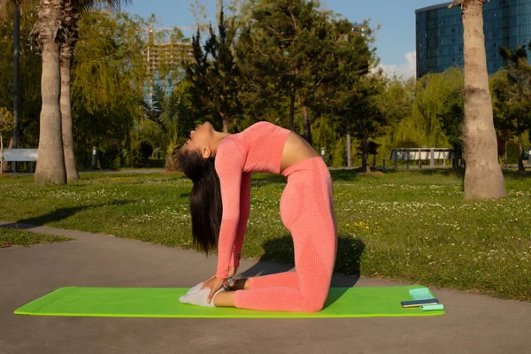 Pembe taytlı güzel siyah bir kadın ve şehir parkında yoga yapan bir kadın..