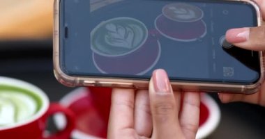Kadın akıllı telefonuyla taze latte fotoğrafı çekiyor.