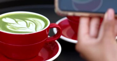 Kadın akıllı telefonuyla taze latte fotoğrafı çekiyor.