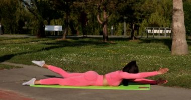 Genç, çok ırklı, pembe spor kıyafetleri, pantolon ve bluz giyen, parkta spor paspası, sağlık sigortası ve zihinsel terapi üzerine yoga egzersizleri yapan çekici bir kadın..