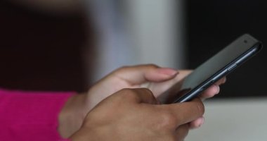 Yan görüş. Evdeki oturma odasında akıllı telefon kullanan ve mesaj yazan bir kız. Genç kadınların yakın plan fotoğrafları..