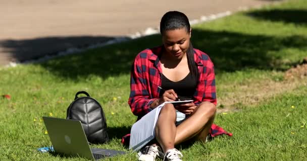 Parktaki Çimenlerde Otururken Elinde Kitap Yazan Neşeli Genç Bir Kadın — Stok video