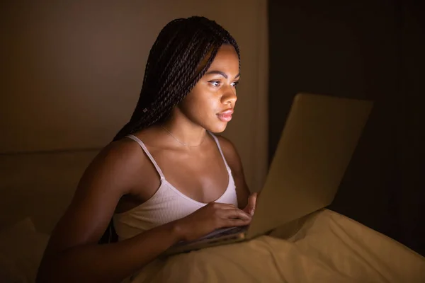 Happy pretty black woman using laptop on bed. Woman using laptop at night.