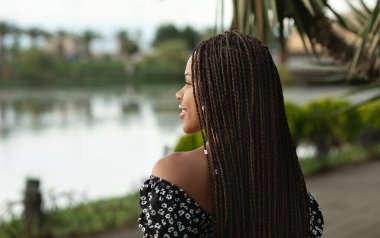 Saçları örgülü, gülümseyen ve cadde boyunca yürüyen güzel Afro-Amerikalı kadın..