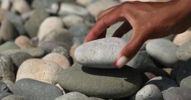 Hand making stone tower on sea beach. Close up of stack of balanced pebbles on beach.