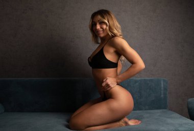 Siyah iç çamaşırlı seksi genç kadın kanepede poz veriyor.