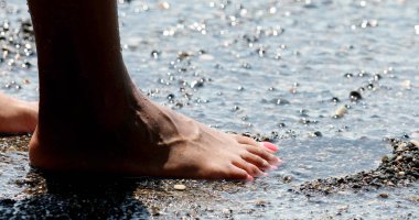 Kayalık bir sahilde duran, ayaklarını yıkayan bir kız. Yaz tatilinde plaj. Yaz konsepti.