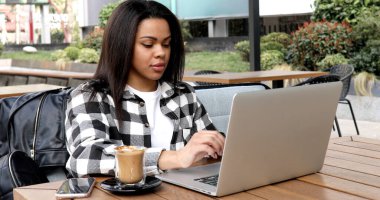 young woman sitting at the table and using laptop computer at street cafe