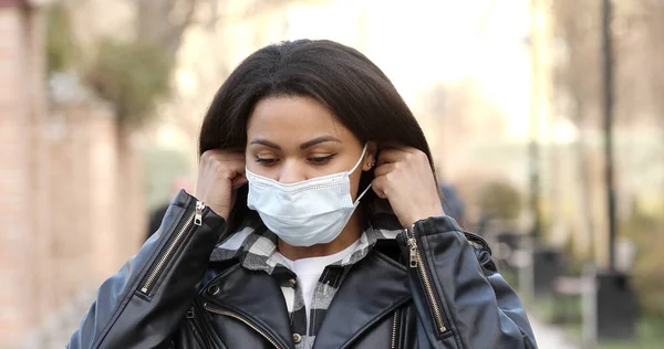 Young woman wearing protective face mask in a city. Masked african-american girl on a city street. Epidemic, pandemic, corona virus protection, healthy lifestyle, people concept.