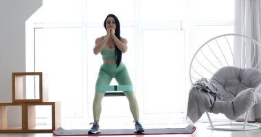 Spor kıyafetli genç bir kadın oturma odasında elastik bantla spor aerobik egzersizleri yapıyor. Ev sağlığı ve sağlık konsepti.