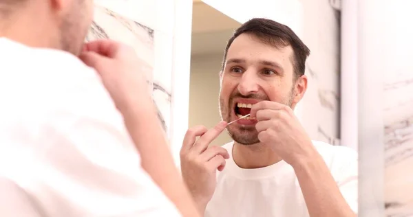 Улыбающийся Молодой Человек Смотрящий Зеркало Использующий Зубную Нить — стоковое фото