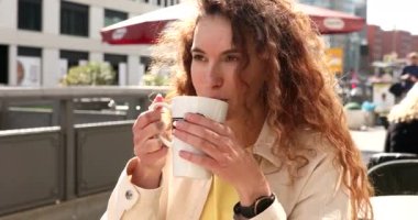 Caddedeki kafede oturan ve fincandan sıcak aromatik kahve içen çekici genç bir kadın.