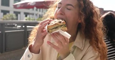 Fast food yiyen genç bir kadın, sandviç, yakın plan. Kafede yemek yiyen bir kadın..